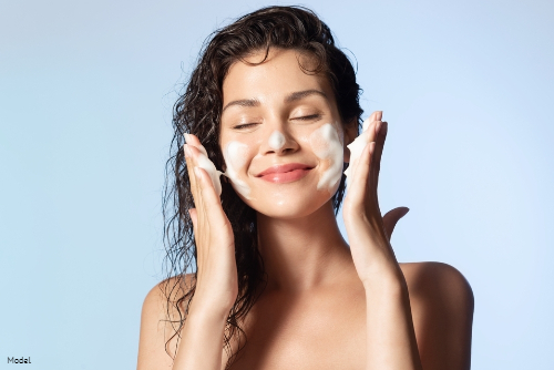 Joyful woman applying a foaming skincare product to her face while smiling